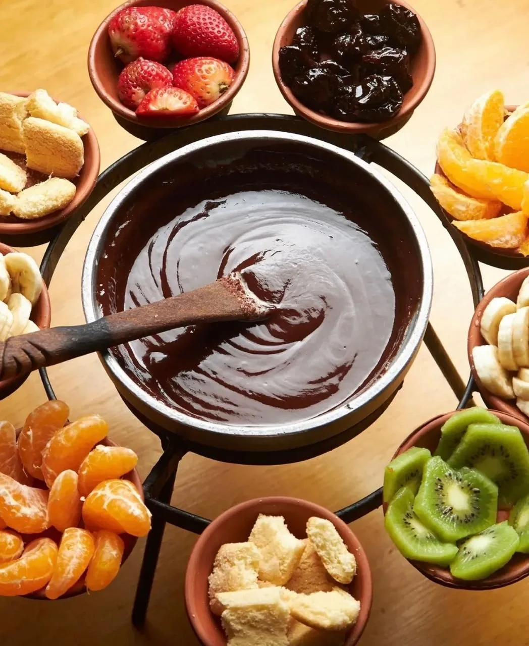 Fondue de chocolate en cazuela, rodeada de frutillas, banana, kiwi, mandarina y bizcochos para mojar.
