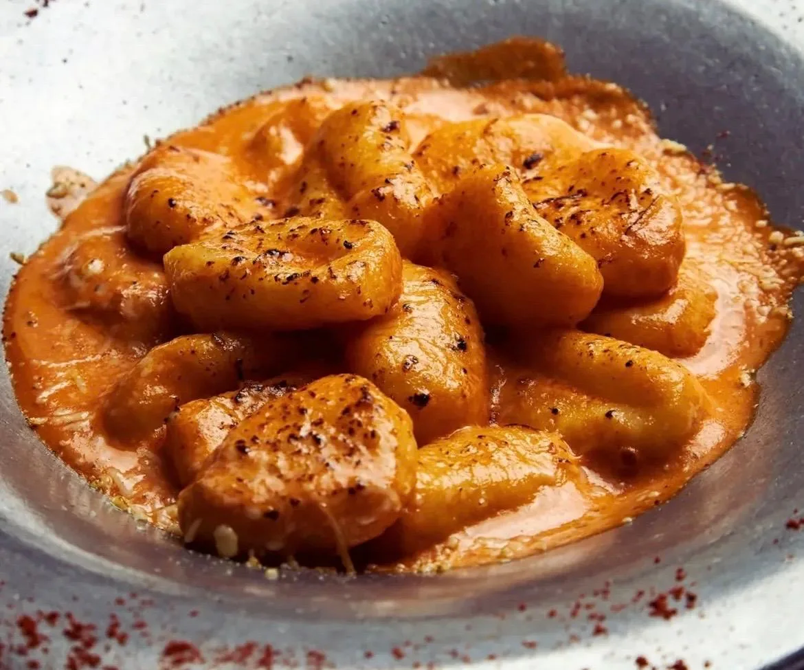 Ñoquis caseros dorados en salsa cremosa de tomate.