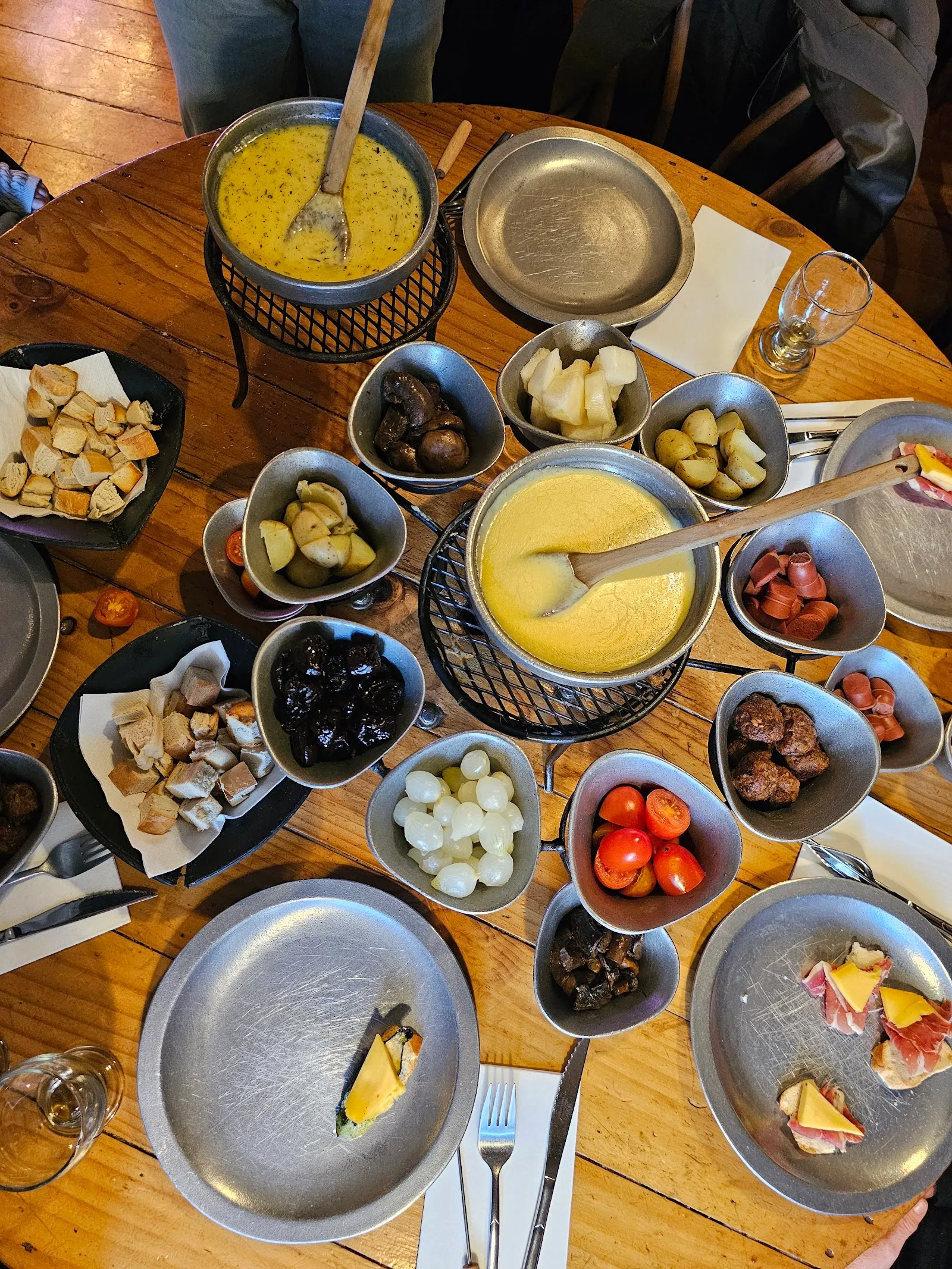 Fondue de queso servida en la mesa con pan, papas y guarniciones para compartir.